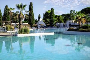 a swimming pool with blue water and palm trees at Belambra Clubs La Grande Motte - Petite Camargue Presqu'île Du Ponant in La Grande Motte