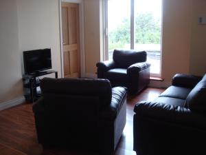 uma sala de estar com um sofá e duas cadeiras e uma televisão em Sun Apartments em Enniscrone