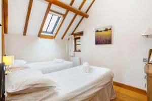 two beds in a room with white walls and wooden ceilings at Shire Cottage in Broadway