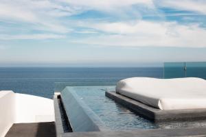 a bed on the edge of a pool with the ocean at Almyra Oia Suites in Oia