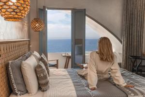 a woman sitting on a bed looking out at the ocean at Almyra Oia Suites in Oia