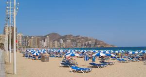 a beach with blue and white chairs and umbrellas at Medplaya Hotel Riudor - Adults Recommended in Benidorm