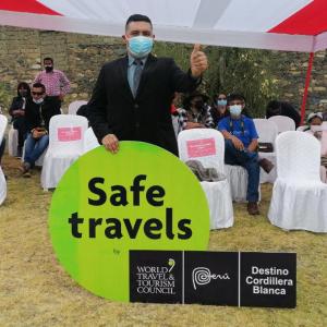 a man wearing a mask holding a sign at a safe travels event at Hotel Residencial Tamia in Huaraz