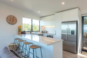 een keuken met witte kasten en een aanrecht met krukken bij Luna Cottage. Stunning ocean views on Waiheke in Oneroa