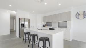 a white kitchen with stools at a white counter at FLOATING ON THE CANALS - 80 COMMODORE CRES in Port Macquarie