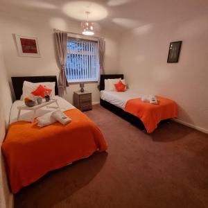 two beds in a room with orange sheets at PREMIER - Whifflet Apartment in Coatbridge