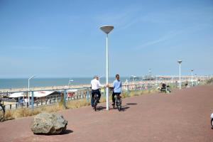 two men riding bikes on a sidewalk near the beach at Hotel Andante aan Zee in Scheveningen