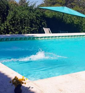 une piscine d'eau bleue avec un parasol bleu dans l'établissement Cabañas Farah Estancia Vieja ideal para 2 a 4 huéspedes, à Villa Carlos Paz