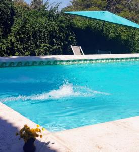 a pool of blue water with a blue umbrella at Cabañas Farah Estancia Vieja ideal para 2 a 3 huéspedes in Villa Carlos Paz