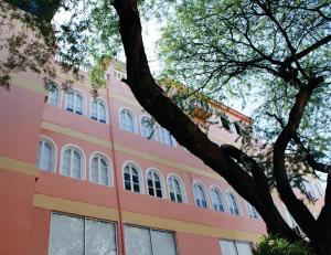 a pink building with white windows and a tree at Hotel Edmar in Santa Marta