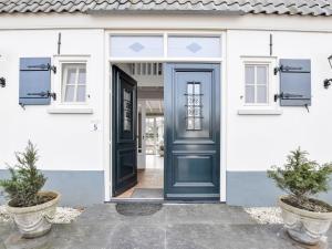 uma porta azul numa casa branca com dois vasos de plantas em Great holiday home at the Efteling with a heated swimming pool and bubble bath in on em Kaatsheuvel