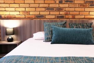 a bed with blue pillows and a brick wall at The Club Motor Inn Chinchilla in Chinchilla