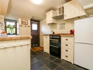 uma cozinha com armários brancos e um forno preto em Gurnard's Cottage em Treen
