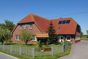 une grande maison avec une clôture devant elle dans l'établissement Hotel-Pension Janssen - Gästehaus Huus an't Deep, à Neuharlingersiel