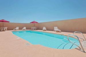 Super 8 by Wyndham Las Cruces/White Sands Area في لاس كروسيس: مسبح وكراسي ومظلات بجانب مبنى