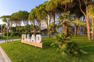 um sinal num parque com palmeiras e um edifício em Fllad Resort & SPA Durres em Golem
