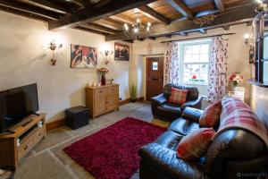 a living room with a leather couch and a television at Poppy Cottage in Grassington