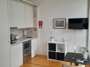 a small kitchen with white cabinets and a table and a television at Great&Cosy São Bento in Porto