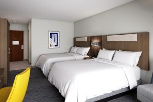 2 Betten in einem Hotelzimmer mit gelbem Stuhl in der Unterkunft Holiday Inn Express & Suites Central Omaha, an IHG Hotel in Omaha