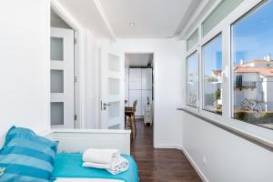 um quarto branco com um sofá azul e janelas grandes em Tilias Apartment at Estoril em Estoril
