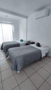 two beds in a white room with a window at Hogar tranquilo, cerca de marina y plaza comercial in Mazatlán