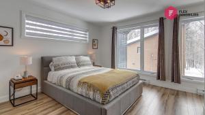 a bedroom with a bed and two large windows at La Fleur Urbaine de Portneuf : 2.5 bathrooms, Hot tub, Sauna and Pool in Pont-Rouge