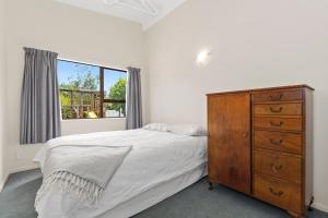 een slaapkamer met een bed, een dressoir en een raam bij Taranui Escape - Mangawhai Heads Holiday Home in Mangawhai