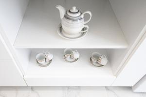 a white cupboard with four cups and a teapot at White home in Timişoara