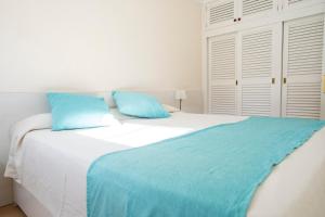a white bed with blue pillows in a bedroom at Orquideas in Cala Galdana