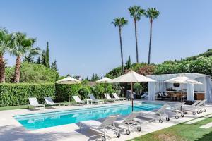 - une piscine avec des chaises longues et des parasols dans l'établissement Villa Tuscany, à Marbella