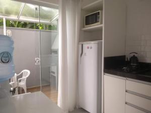 eine weiße Küche mit einem Kühlschrank und einem Tisch und einem Fenster in der Unterkunft Residencial Farol das Conchas in Bombinhas