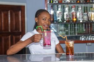 a woman sitting at a bar holding a drink at Elephant View Lodge & Apartments in Livingstone