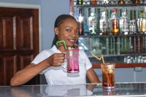 una mujer sentada en un bar sosteniendo una bebida en Elephant View Lodge & Apartments, en Livingstone