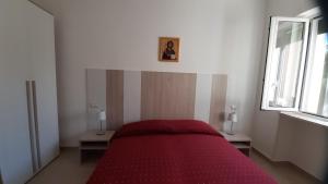 ein rotes Bett in einem weißen Zimmer mit Fenster in der Unterkunft Trullo dell'Immacolata - Casa vacanze gestita da suore in Selva di Fasano