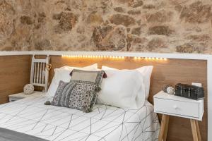 a bedroom with a bed with white pillows and a stone wall at Casa Trilhos da Serra in Alcobertas