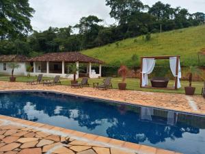 a swimming pool with chairs and a gazebo at HOTEL FAZENDA PACIENCIA in Santana dos Montes