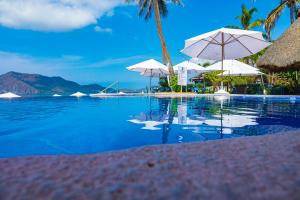 a swimming pool with white umbrellas and the ocean at Mar Celeste in Manzanillo
