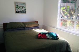 a bedroom with a bed with a green comforter and two windows at Frangipani guesthouse -Ngunguru in Whangarei