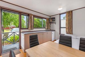 a dining room with a table and chairs and windows at Hamilton City Holiday Park in Hamilton