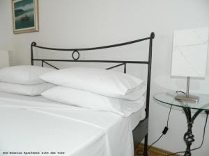 Cama con almohadas blancas y mesa con lámpara en Pink Inn, en Podstrana