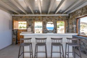 a kitchen with a bar with chairs and windows at Ethereal Villa Mykonos in Kalafatis