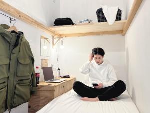 une femme assise sur un lit en regardant son téléphone portable dans l'établissement Blue Hour Kanazawa, à Kanazawa