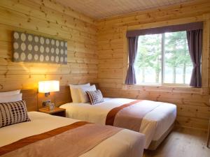 two beds in a log cabin bedroom with a window at The Prince Villa Karuizawa in Karuizawa