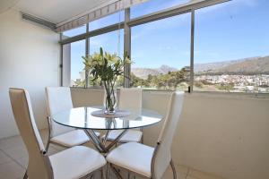 a glass table with white chairs and a vase with flowers at Sandringham in Cape Town