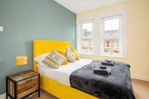 a bedroom with a bed with a yellow headboard and two windows at Fantastic, Spacious 3 Bedroom House With Garden in Bath