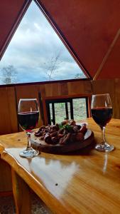 two glasses of wine on a table with a plate of food at Domo Vive Pellaifa in Coñaripe