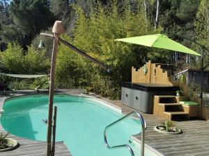 una piscina con una sombrilla verde y una terraza de madera en Les Hôtes Landes, en Saint-Gor