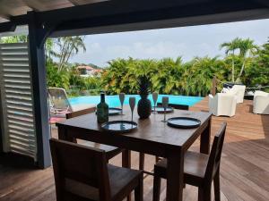 a wooden table and chairs on a deck with a pool at Magnifique Villa Domaine de Biglette in Baie-Mahault