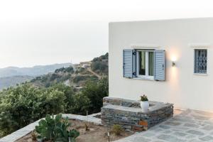 ein weißes Haus mit einem blauen Fenster und Bergen in der Unterkunft Cycladic Villa with sea view! in Ioulis