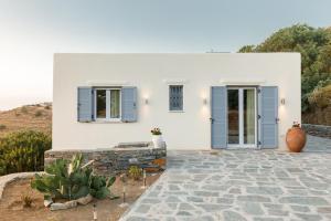 a white house with blue shutters on it at Cycladic Villa with sea view! in Ioulida